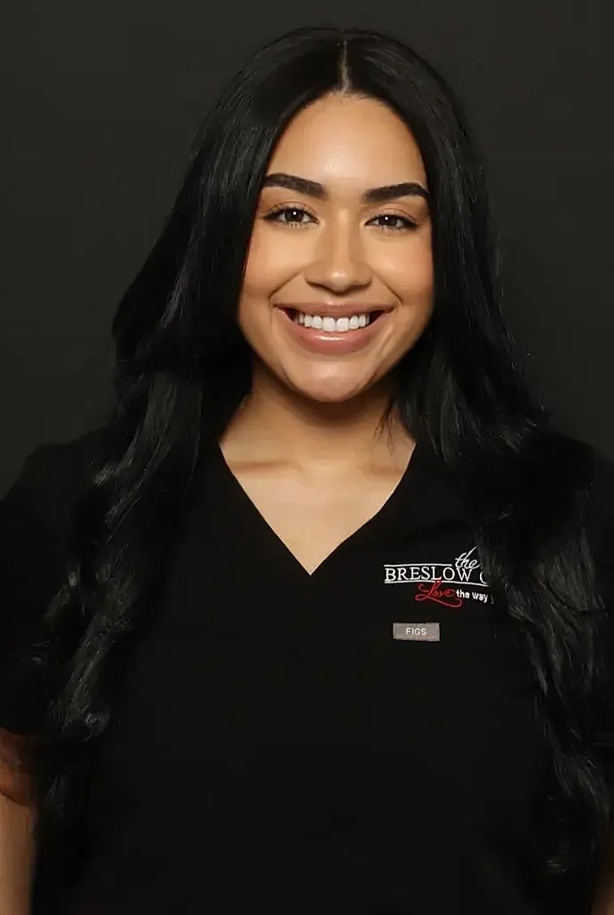 Smiling woman in medical scrubs against black background.