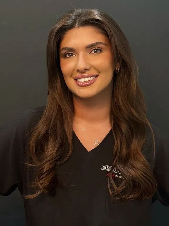 Smiling woman in medical attire against dark background.