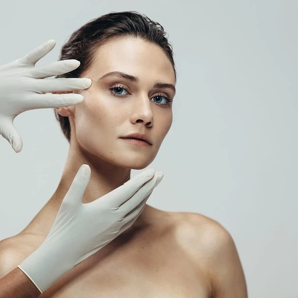 Model with gloved hands touching her face.