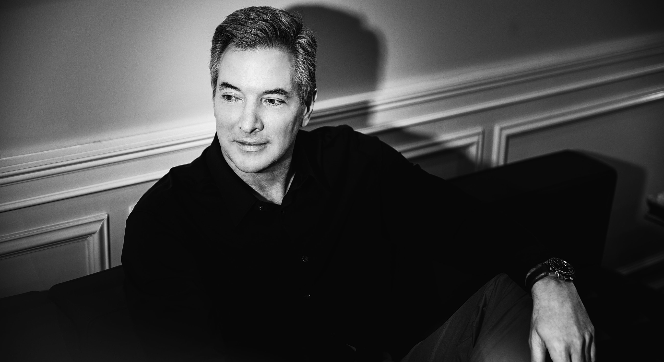 Man in black shirt, seated with thoughtful expression.