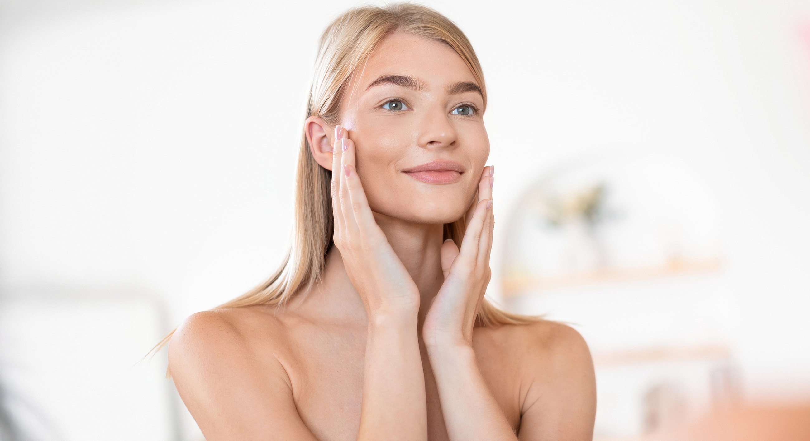 Woman applying skincare in bright, minimalist setting.