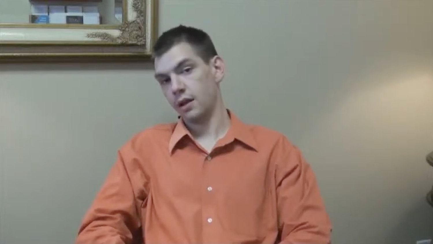 Person seated in an orange shirt, thoughtful expression.