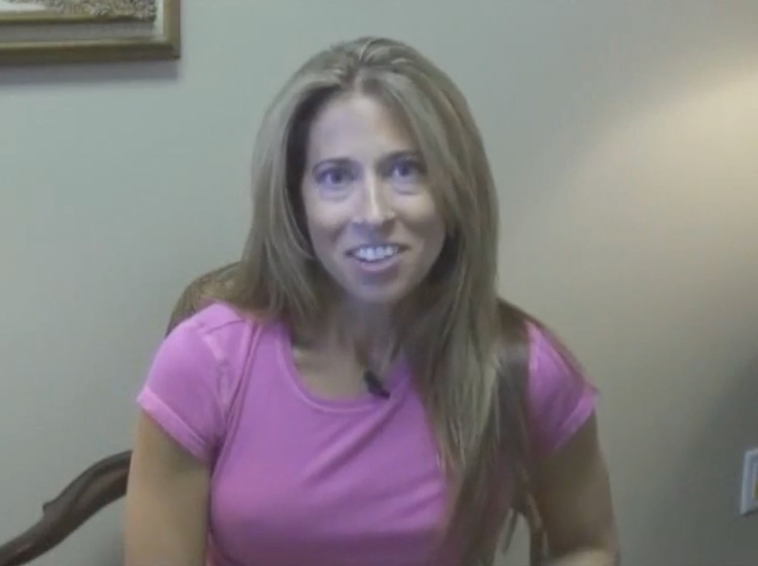 Smiling woman wearing a pink shirt indoors.